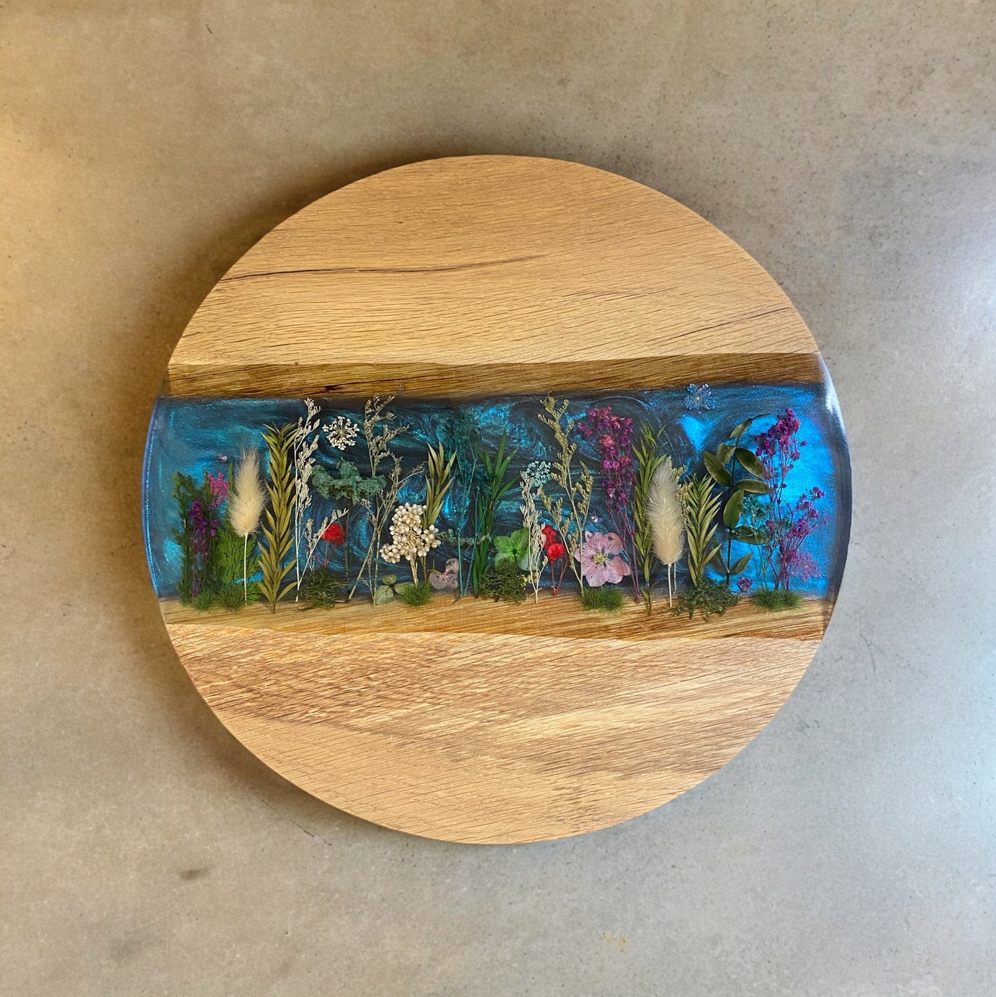 A handcrafted oak and epoxy resin end table featuring a chameleon-coloured background with real dried flowers arranged to resemble a meadow.