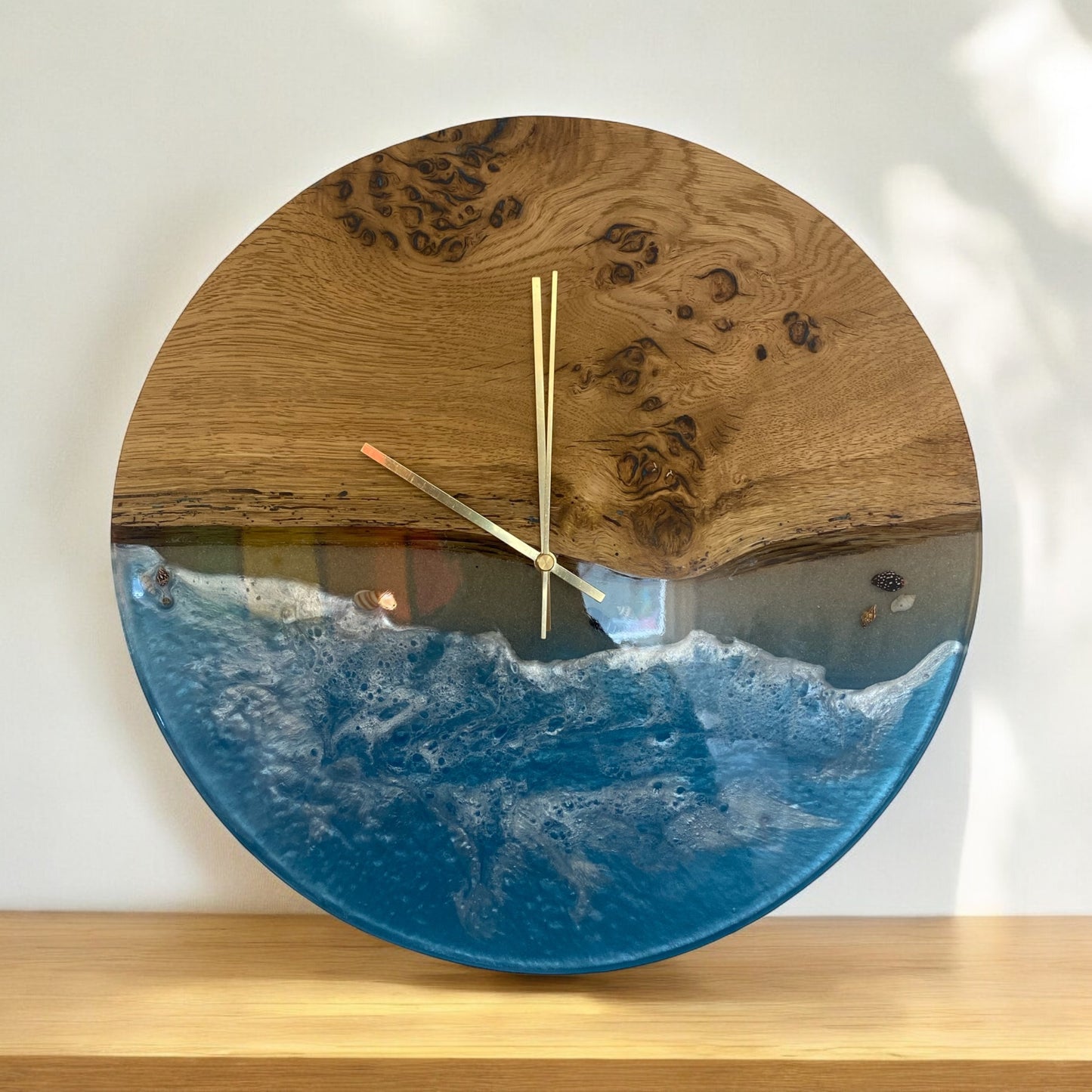 Handcrafted oak and epoxy wall clock with a serene ocean wave effect in deep blue hues, gold clock hands, and a silent quartz movement.