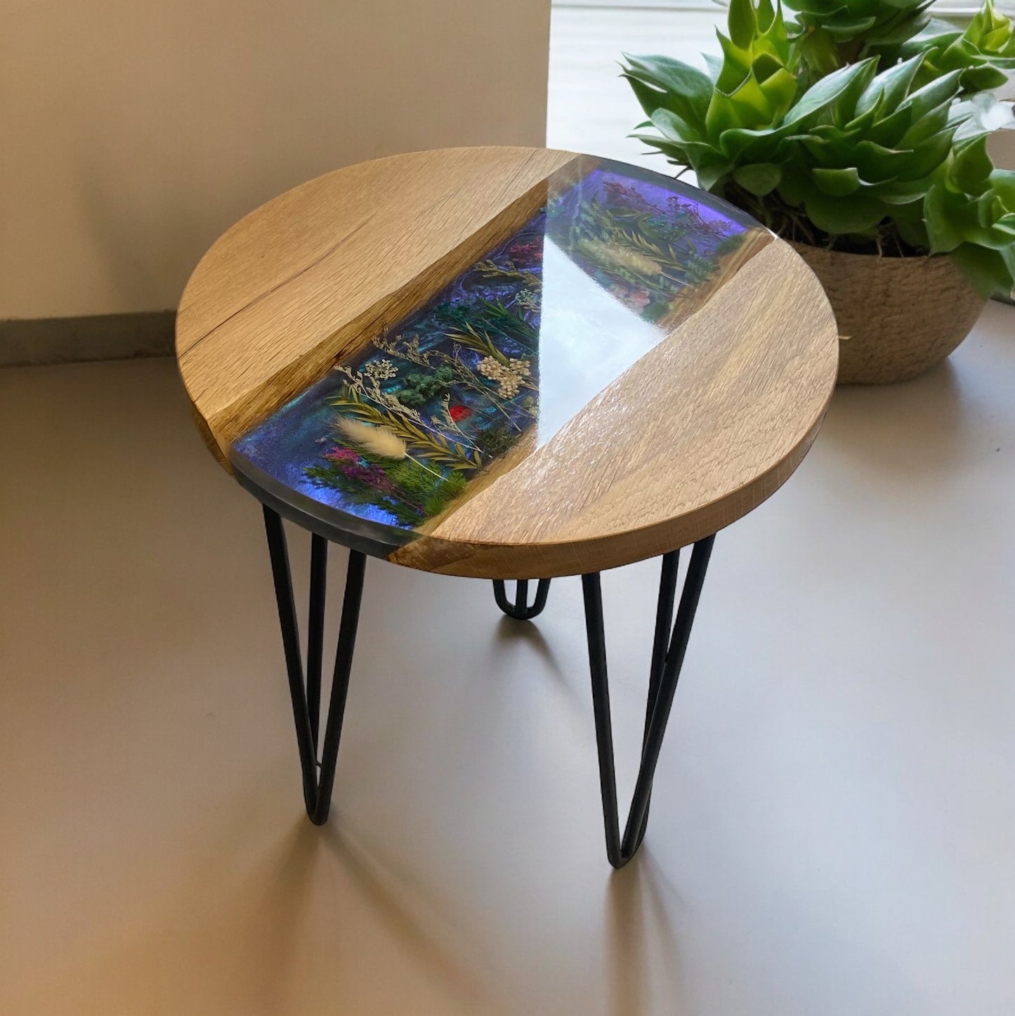 A detailed view of the oak and resin end table, with a dynamic colour-changing background enhancing the beauty of the dried flowers.