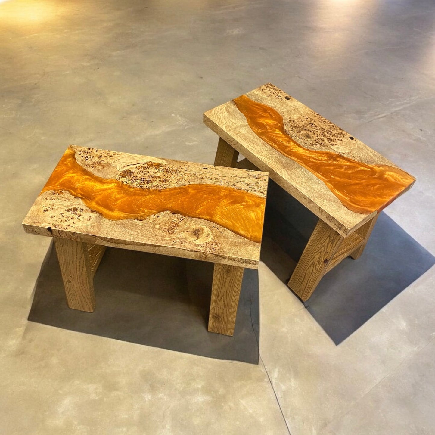 A pair of orange resin river tables made from live edge oak. hey have solid oak a frame legs