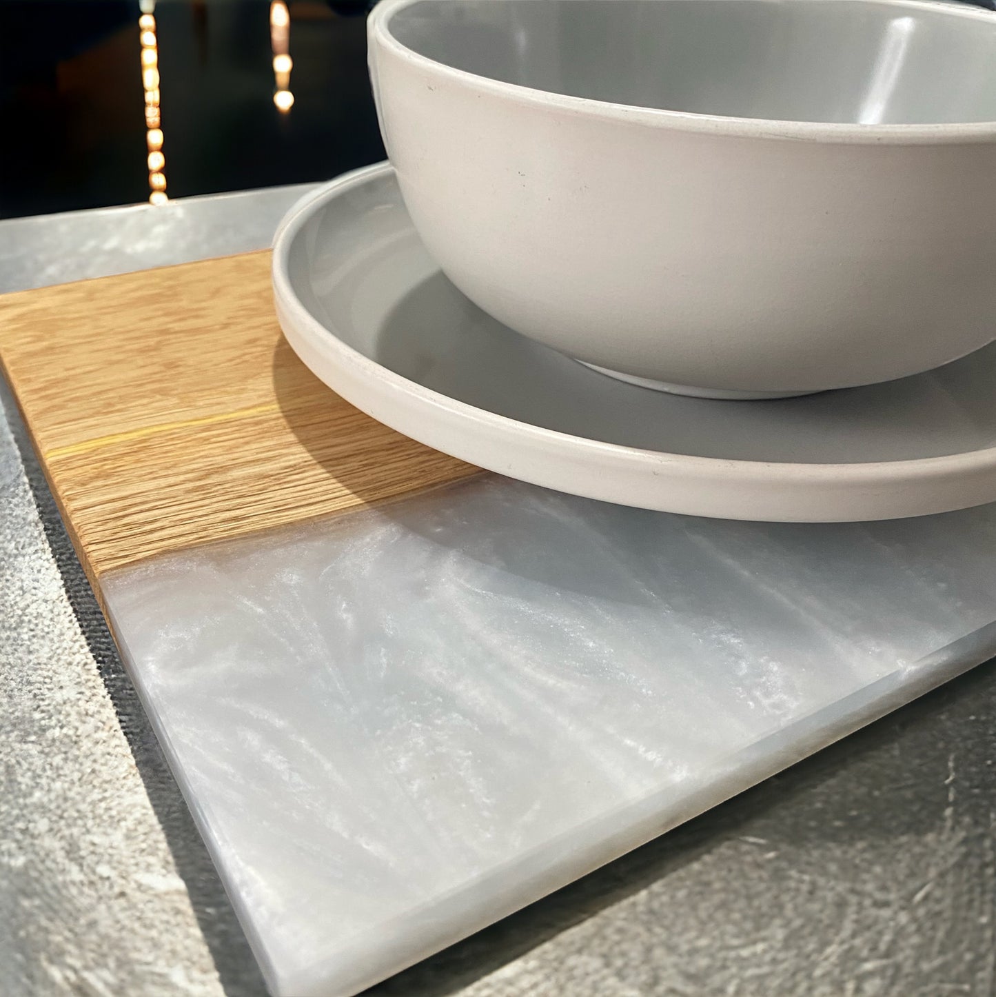 a close up of a plate and bowl stacked on top of an oak and white rein placemat sat on a marble worktop