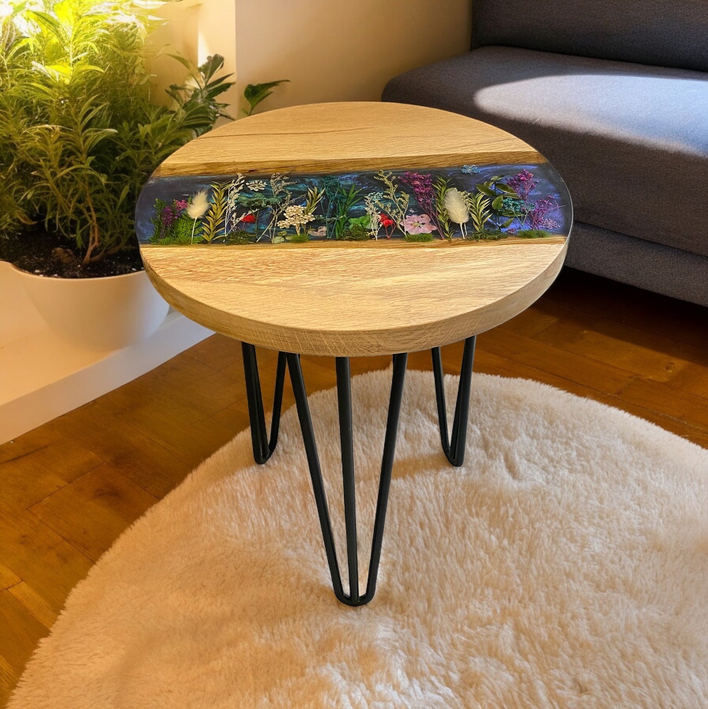 A beautiful round, oak and epoxy resin end table. With an epoxy resin river that features a blue background and dried flower, meadow style design.