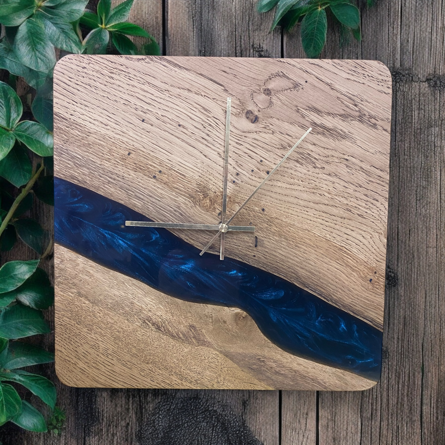 Square oak and epoxy resin wall clock with a striking astral blue resin design, gold metal hands, and a sleek minimalist aesthetic