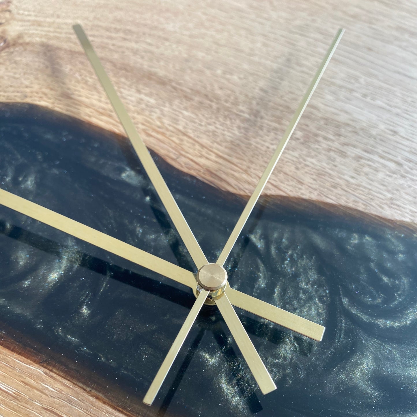 Close-up of oak and epoxy resin clock face, showing sleek gold hands and green-black resin detail.