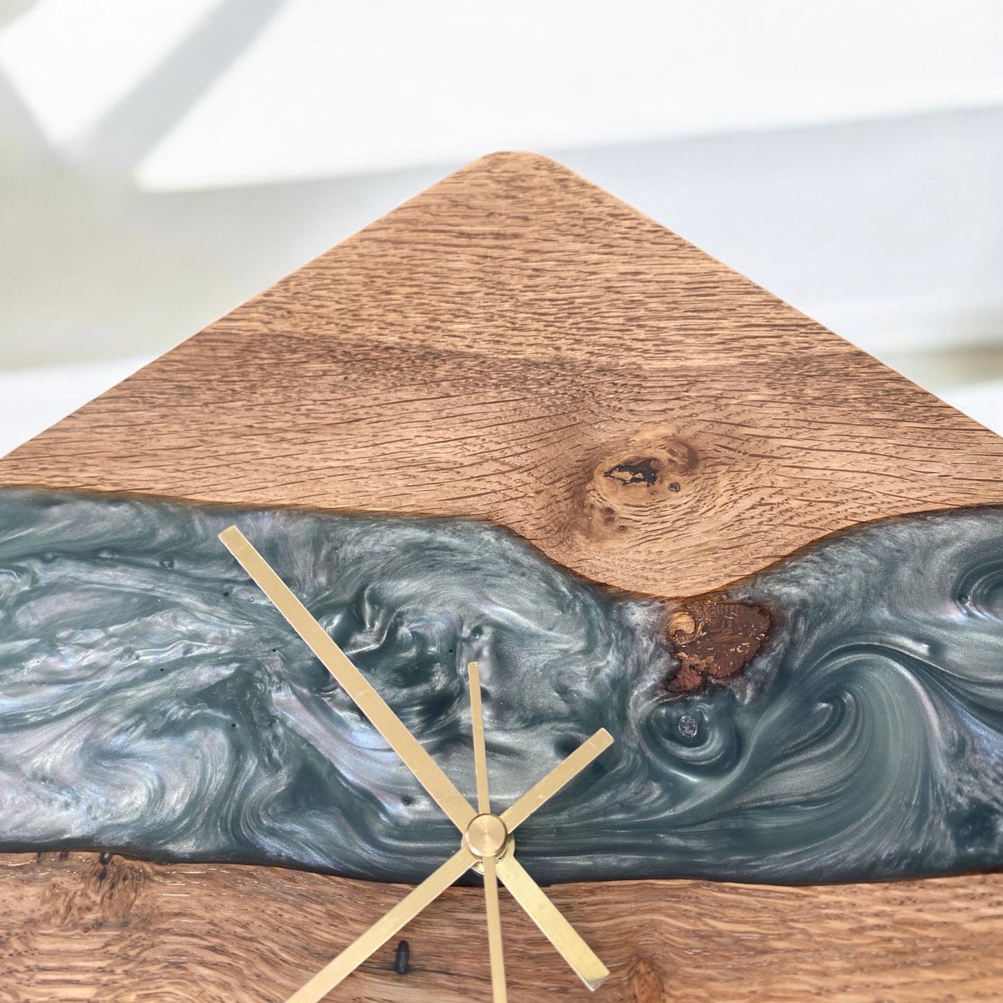 Close-up of the oak and Sage Green epoxy resin clock face, highlighting the intricate wood grain, smooth resin finish and gold metal clock hands.