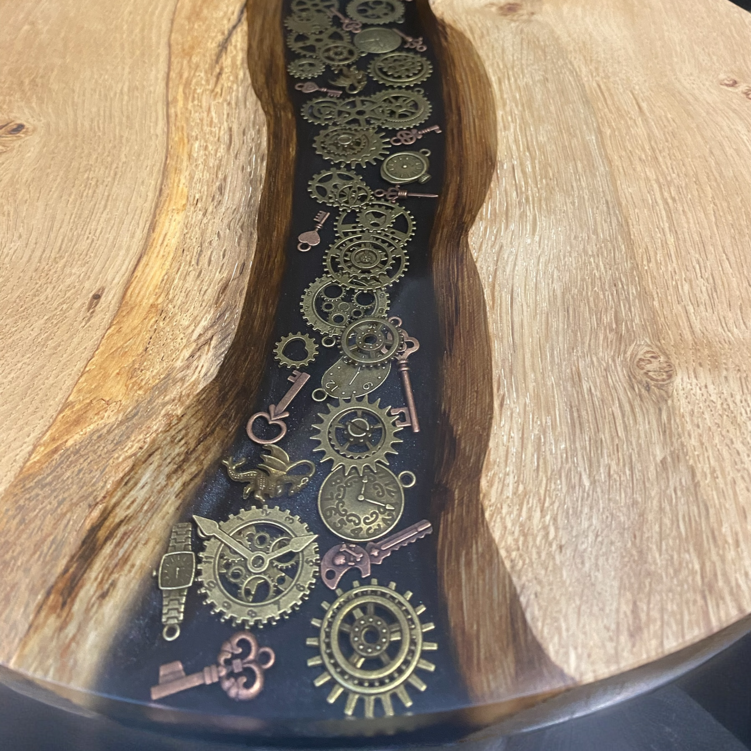 Close-up of the epoxy resin surface showcasing embedded steampunk gears and cogs in gold and bronze tones against a deep, smoky background.