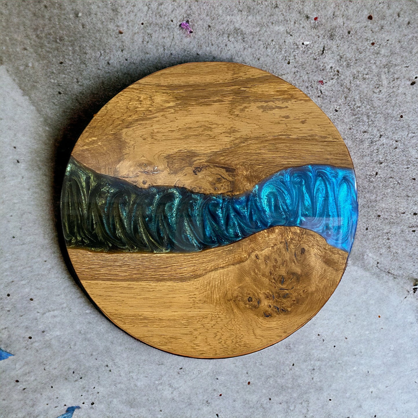 A round oak and epoxy resin end table featuring a striking peacock green and blue resin swirl, enhancing the natural wood grain.