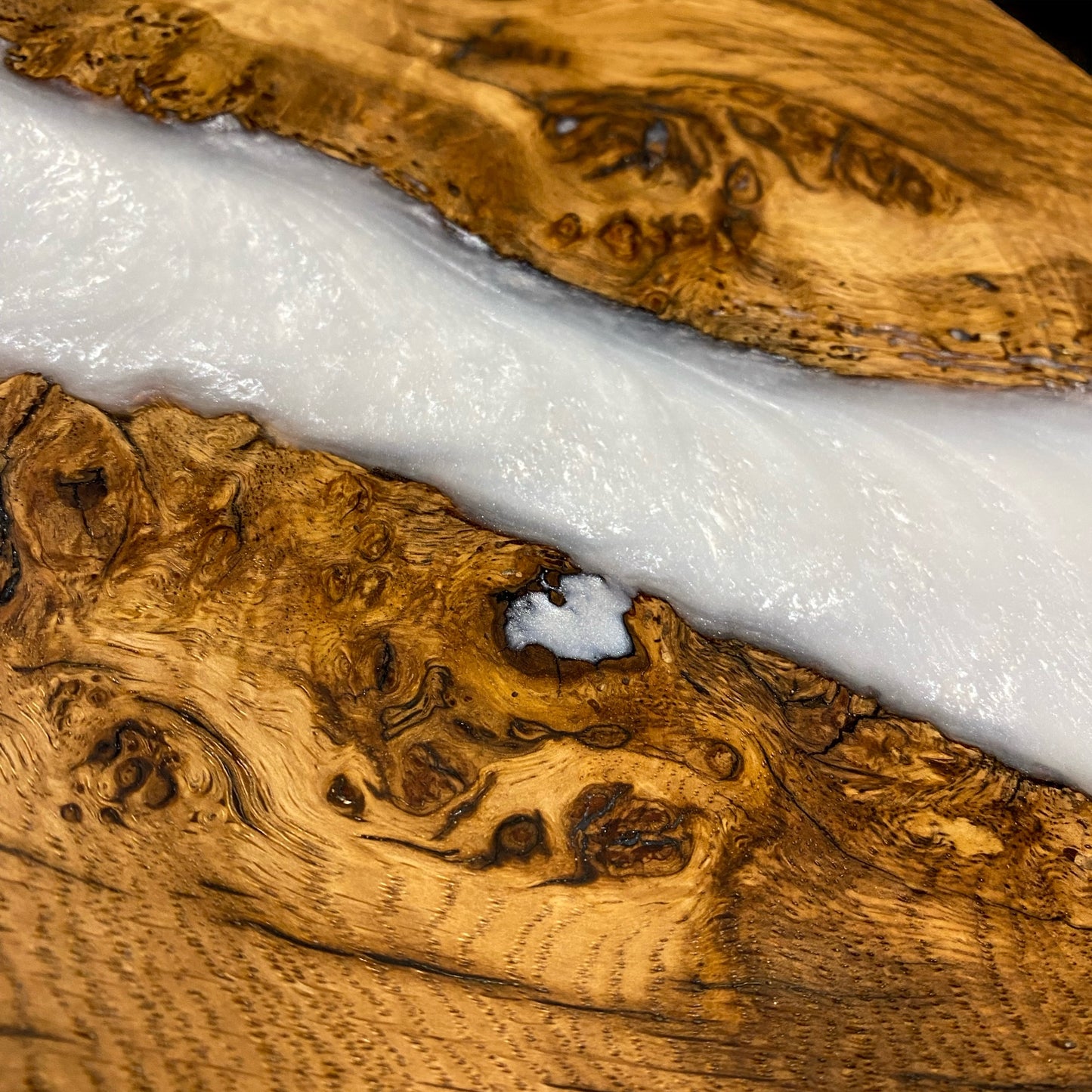 A detailed close-up of the dark oak and snow-white resin table top, showing the natural wood grain and high-gloss resin finish.