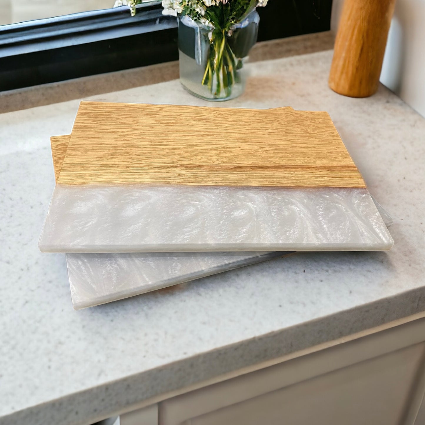 2 oak and white resin placemats sat on a white granite worktop with a window and a vase of flowers in the background