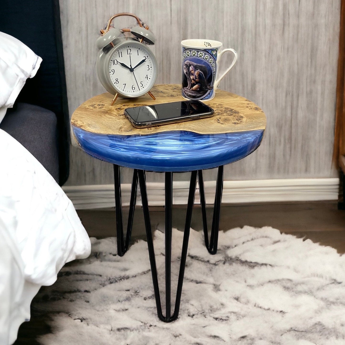 Denim blue epoxy resin end table styled as a bedside table, holding an alarm clock, cup, and phone for a cosy bedroom setup.